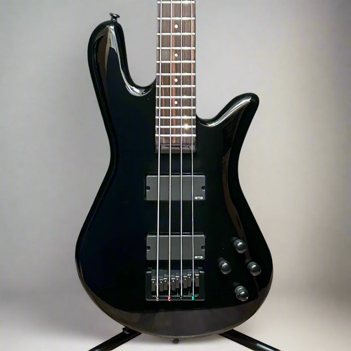 Black electric bass guitar on a wooden stand against a wooden background