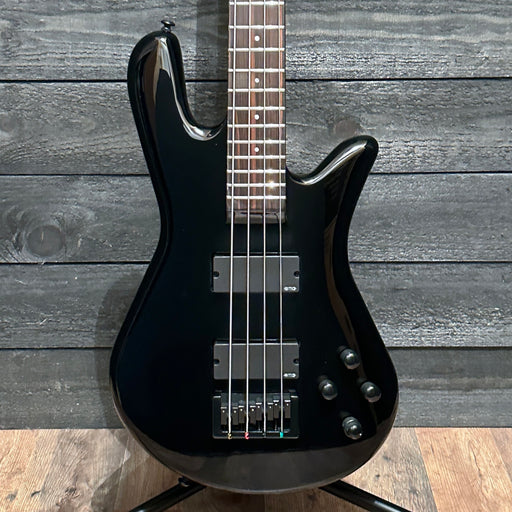 Black electric bass guitar on a wooden stand against a wooden background